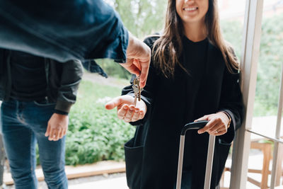 Cropped hand of owner giving house keys to woman while standing with friend at doorway