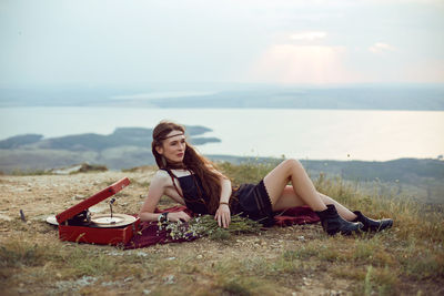 Young woman lies in nature in a black dress next to an old gramophone and listens to music