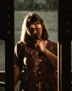 Portrait of a young woman on ledge of wooden cabin at sunset