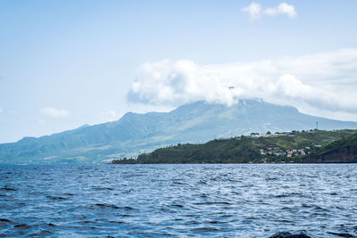 Scenic view of sea by mountain against sky