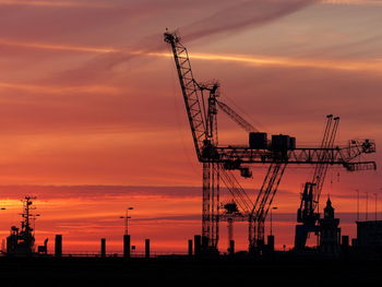 Silhouette cranes against sky at sunset