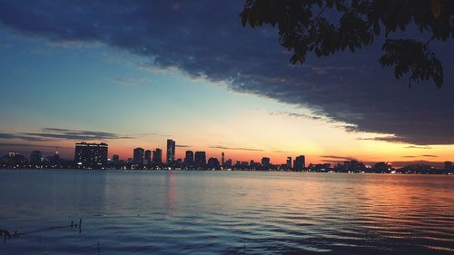 Sea by illuminated city against sky at sunset