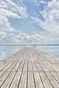 Pier amidst river against cloudy sky during sunny day