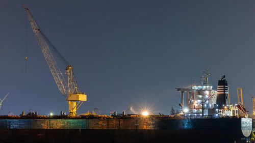 Illuminated cranes at commercial dock against sky at night