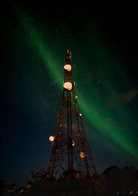 Low angle view of communications tower against sky at night with aurora borealis