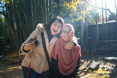 Portrait of smiling young woman standing against trees