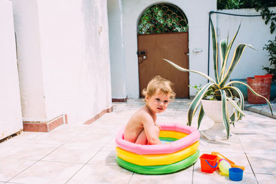 Cute child has fun in inflatable pool with toys in summer in backyard.