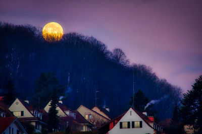 Silhouette trees and buildings against full moon