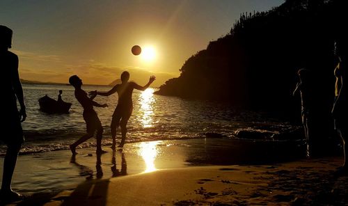 Silhouette friends playing on shore at beach