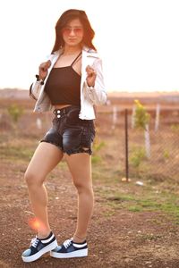 Portrait of young woman standing on field against sky