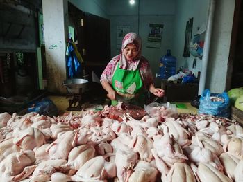 Smiling young woman cutting chicken meat while standing at market stall