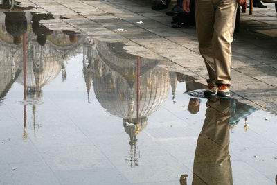 Low section of man standing by puddle on street