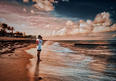 Rear view of woman walking at beach against sky during sunset