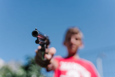 Blonde teenager wearing a red t - shirt pointing with a gun.