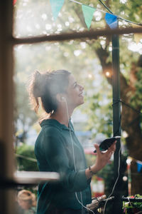 Smiling young woman looking up while talking through earphones in balcony during party