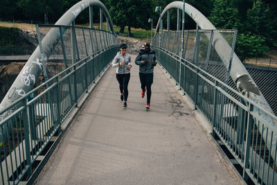 Full length of male and female friends jogging on footbridge in city