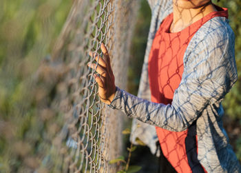 Midsection of woman standing by fence on field