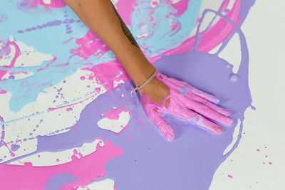 Woman pours blue paint from a jug on her body sitting on a white canvas in the studio