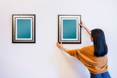 Rear view of woman hanging blank picture frame on wall