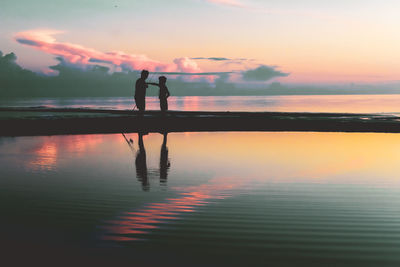 Rear view of man standing at beach against sky during sunset