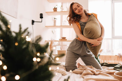 A pretty girl in pajamas rejoices and smiles during christmas holidays in a cozy bedroom interior