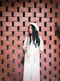 Young woman standing against brick wall