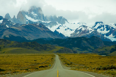 Scenic view of road leading snowcapped mountains against sky