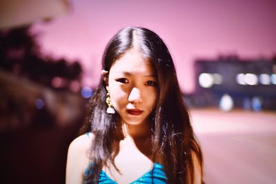 Portrait of beautiful young woman against illuminated sky