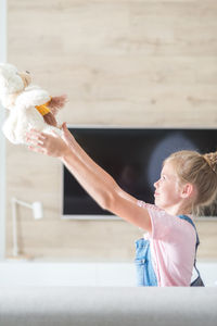 Side view of girl playing with teddy bear at home