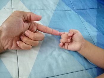 Cropped hands of parent and baby on bed