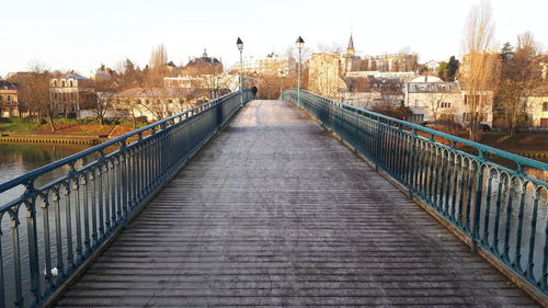 Footbridge over river amidst buildings in city against sky