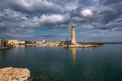 Buildings by sea against cloudy sky