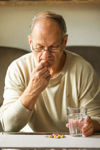 Caucasian senior man taking red and yellow capsule in his mouth and drinking water from glass.