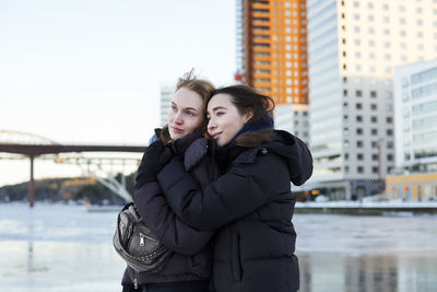 Young women standing at river in winter and hugging