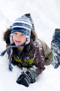 Portrait of cute boy lying on snow covered land