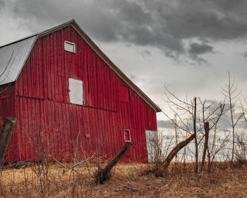 Red barn on field by building against sky