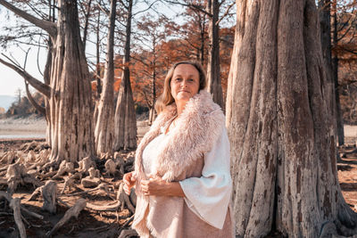 Woman standing by tree trunk in forest during winter
