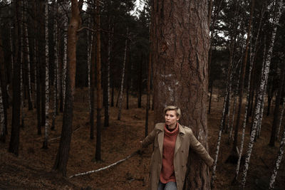 Portrait of woman standing by tree trunk in forest