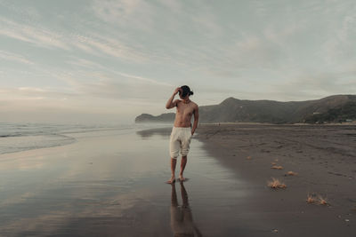 Rear view of woman walking at beach against sky during sunset