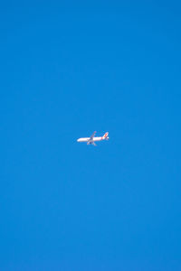 Low angle view of airplane flying against clear blue sky