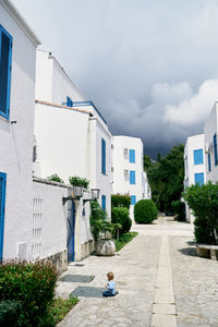 Rear view of man walking amidst buildings in city against sky