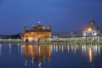 Illuminated golden temple by lake against sky at dusk