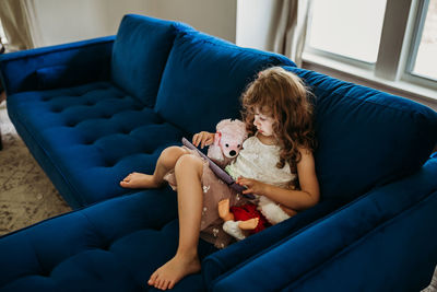 Young girl sitting inside on blue couch using tablet