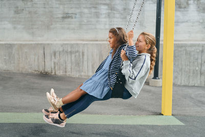 Full length of carefree sisters swinging together on swing at playground