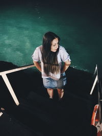 High angle view of young woman standing on steps against swimming pool