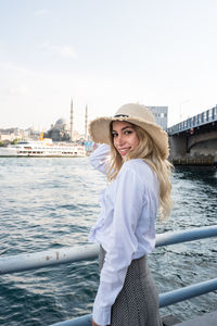 Portrait of happy young woman standing against river in city