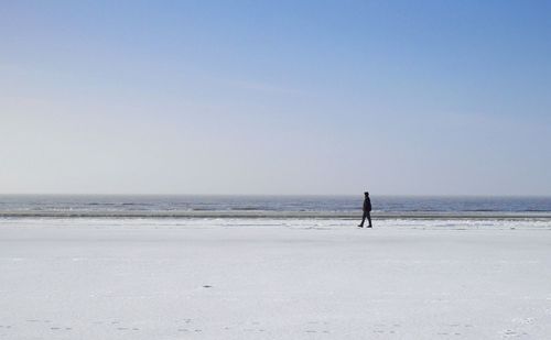 Side view of man walking at snowcapped beach during winter