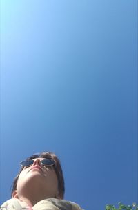 Low angle view of woman wearing sunglasses against clear blue sky