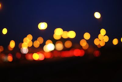 Defocused image of illuminated lights against sky at night