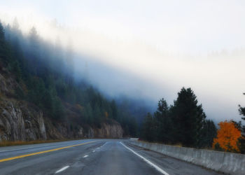 Road by trees on mountain against sky